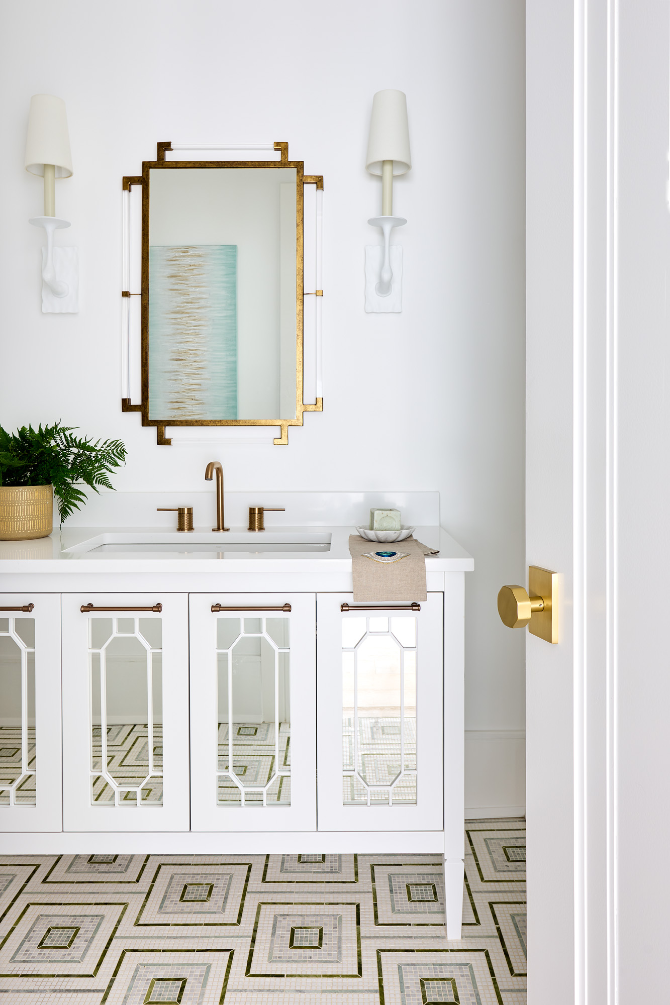 Highgate estate powder bath — brass-framed mirror, mirrored fretwork vanity, and custom mosaic tile floor