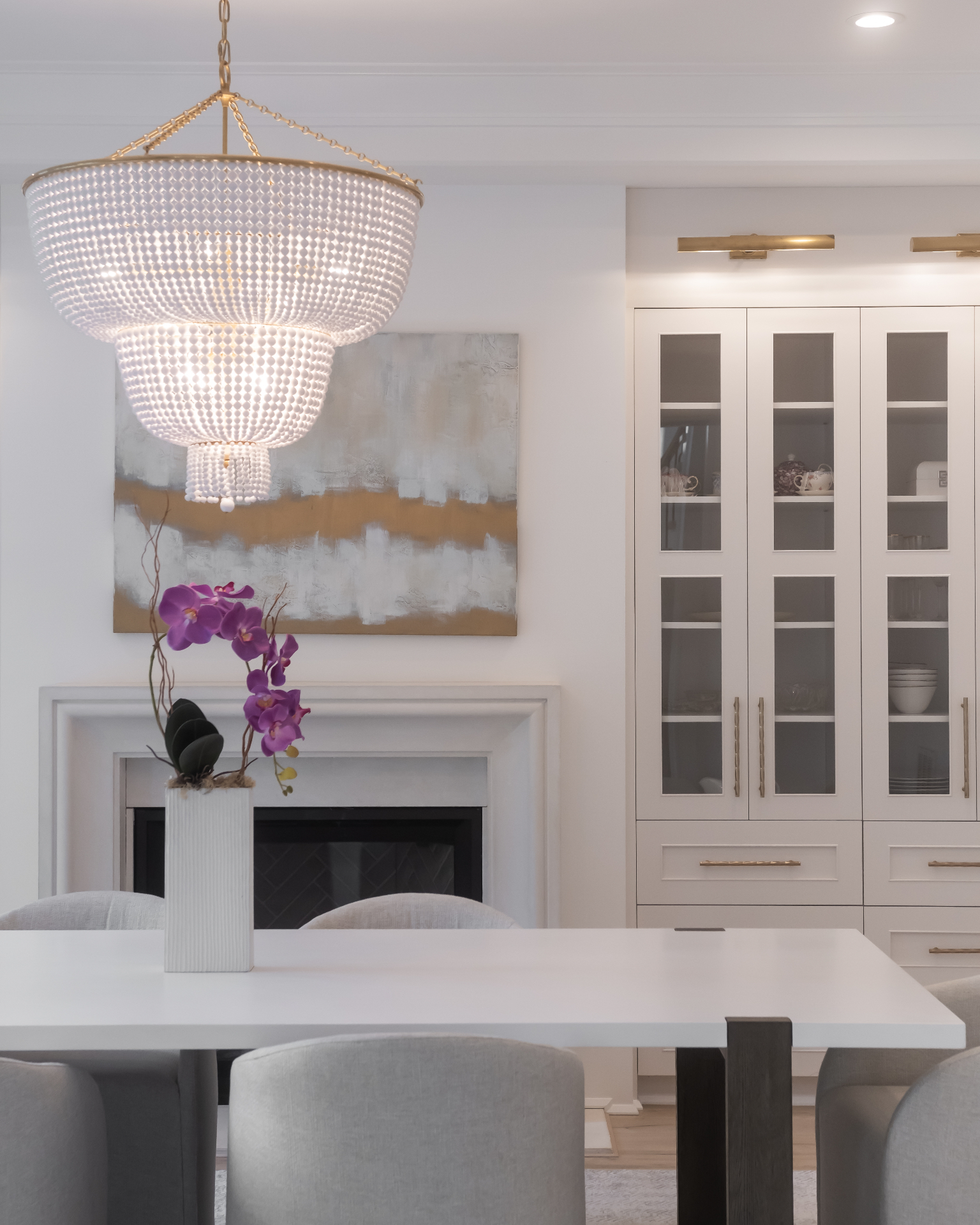 Formal dining room in a Highgate estate — two-tier beaded chandelier, cast-stone fireplace, and ivory glass-front china cabinets